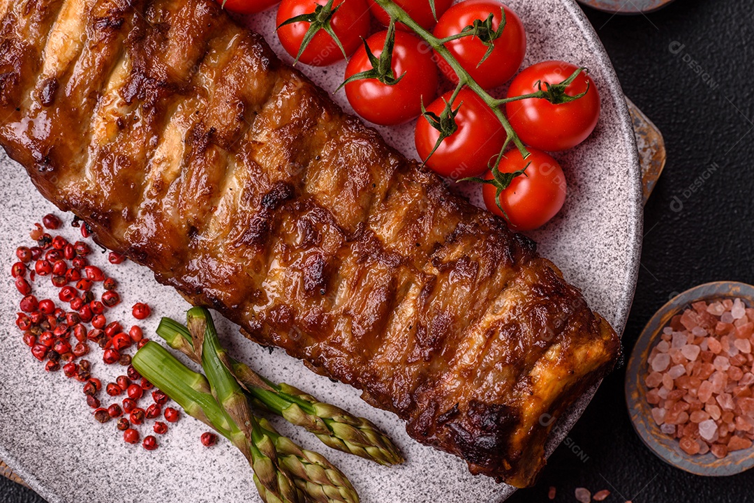 Deliciosas costelas grelhadas suculentas com mel e molho de mostarda com sal, especiarias e ervas sobre um fundo escuro de concreto