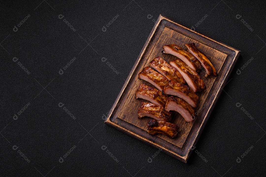 Deliciosas costelas grelhadas suculentas com mel e molho de mostarda com sal, especiarias e ervas sobre um fundo escuro de concreto