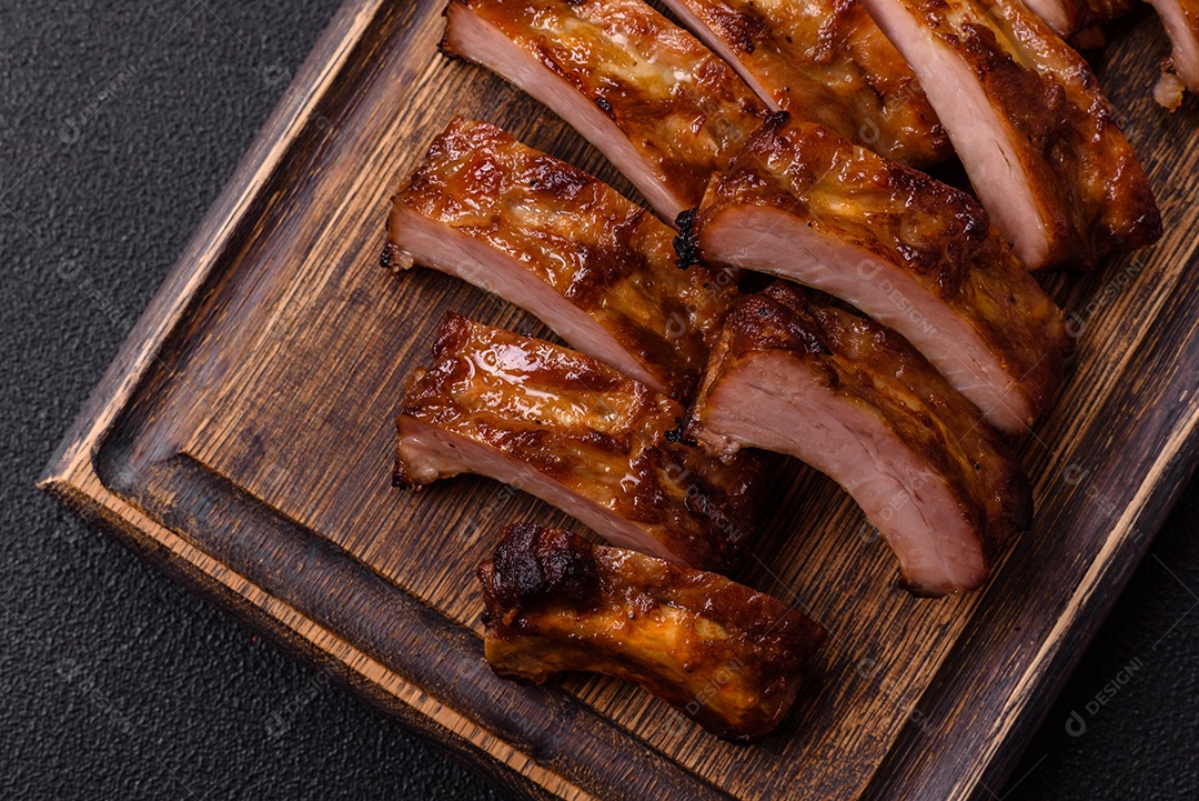 Deliciosas costelas grelhadas suculentas com mel e molho de mostarda com sal, especiarias e ervas sobre um fundo escuro de concreto