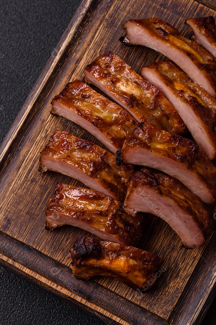 Deliciosas costelas grelhadas suculentas com mel e molho de mostarda com sal, especiarias e ervas sobre um fundo escuro de concreto