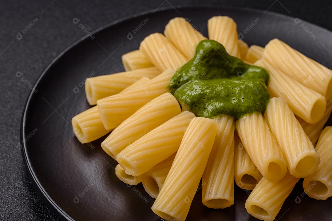 Deliciosa massa com molho de espinafre, azeite e queijo parmesão com sal, especiarias e ervas sobre fundo escuro de concreto