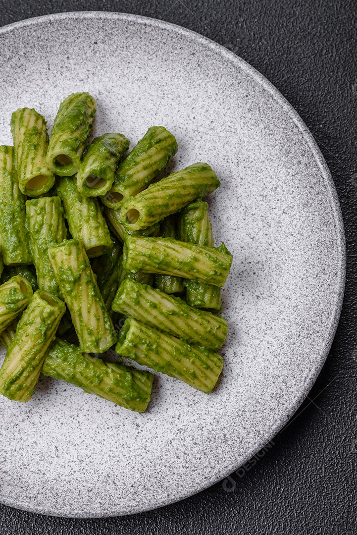 Deliciosa massa com molho de espinafre, azeite e queijo parmesão com sal, especiarias e ervas sobre fundo escuro de concreto