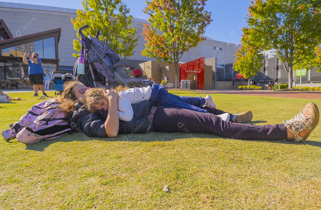 Mãe e filha se abraçando deitadas na grama do parque