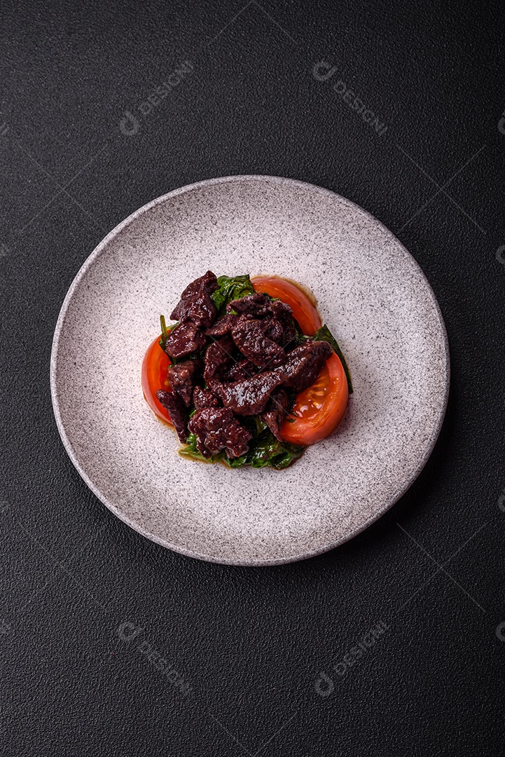 Deliciosa salada quente de fígado de galinha, espinafre, rúcula, tomate com sal, especiarias e ervas sobre um fundo escuro de concreto