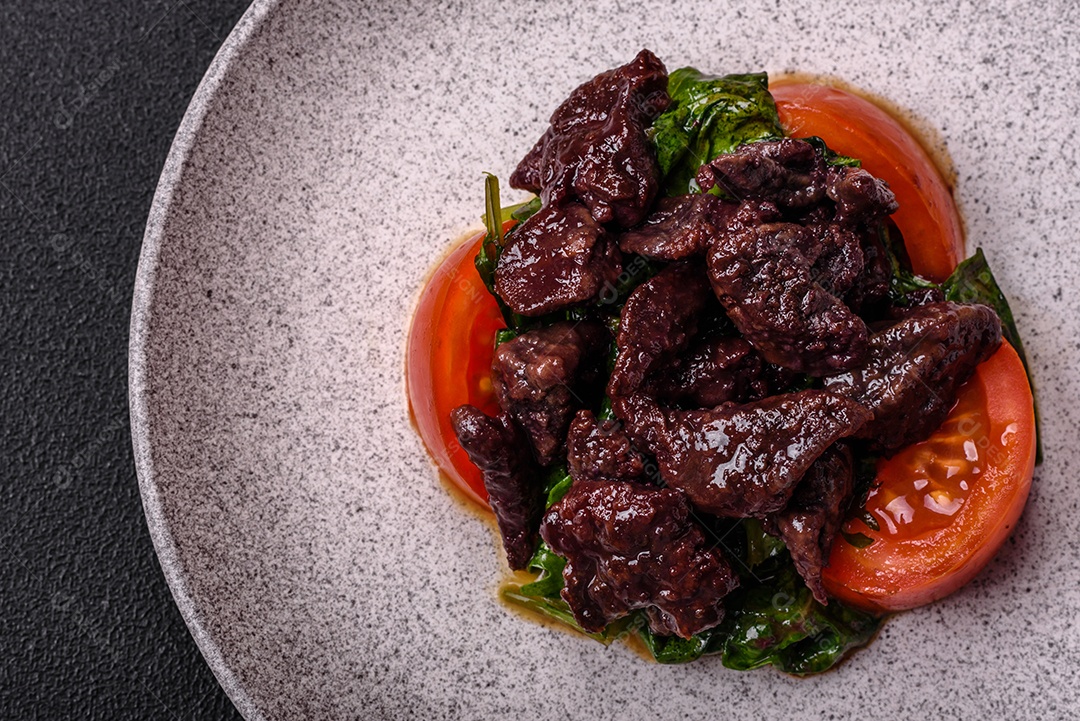 Deliciosa salada quente de fígado de galinha, espinafre, rúcula, tomate com sal, especiarias e ervas sobre um fundo escuro de concreto