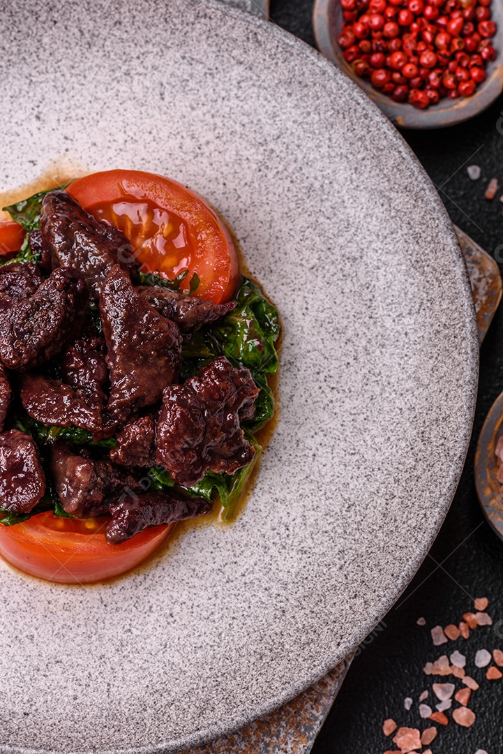 Deliciosa salada quente de fígado de galinha, espinafre, rúcula, tomate com sal, especiarias e ervas sobre um fundo escuro de concreto