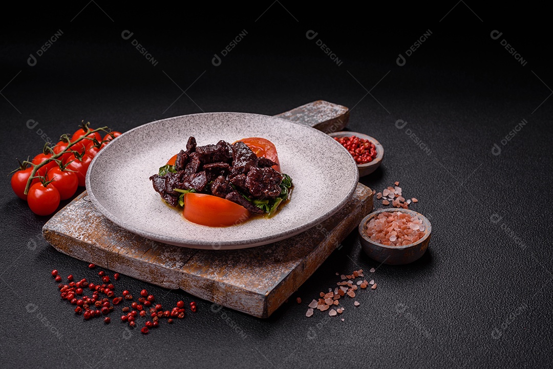 Deliciosa salada quente de fígado de galinha, espinafre, rúcula, tomate com sal, especiarias e ervas sobre um fundo escuro de concreto