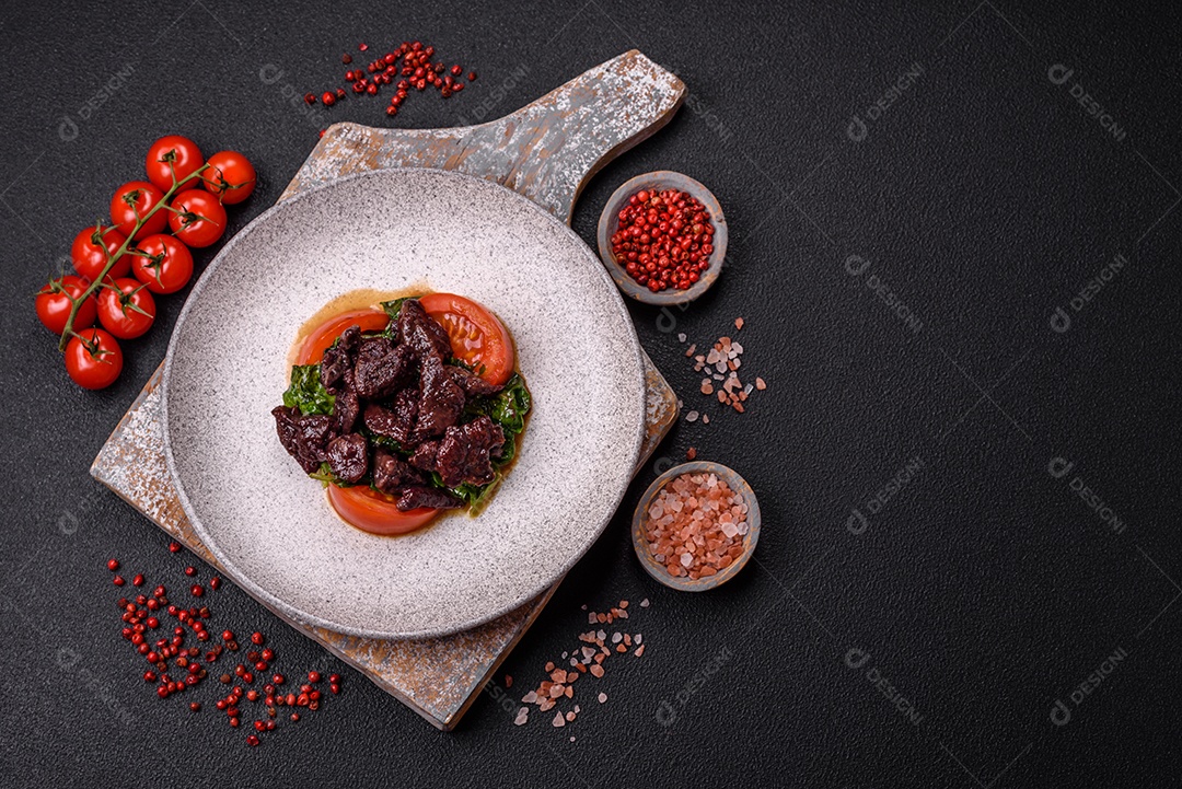 Deliciosa salada quente de fígado de galinha, espinafre, rúcula, tomate com sal, especiarias e ervas sobre um fundo escuro de concreto