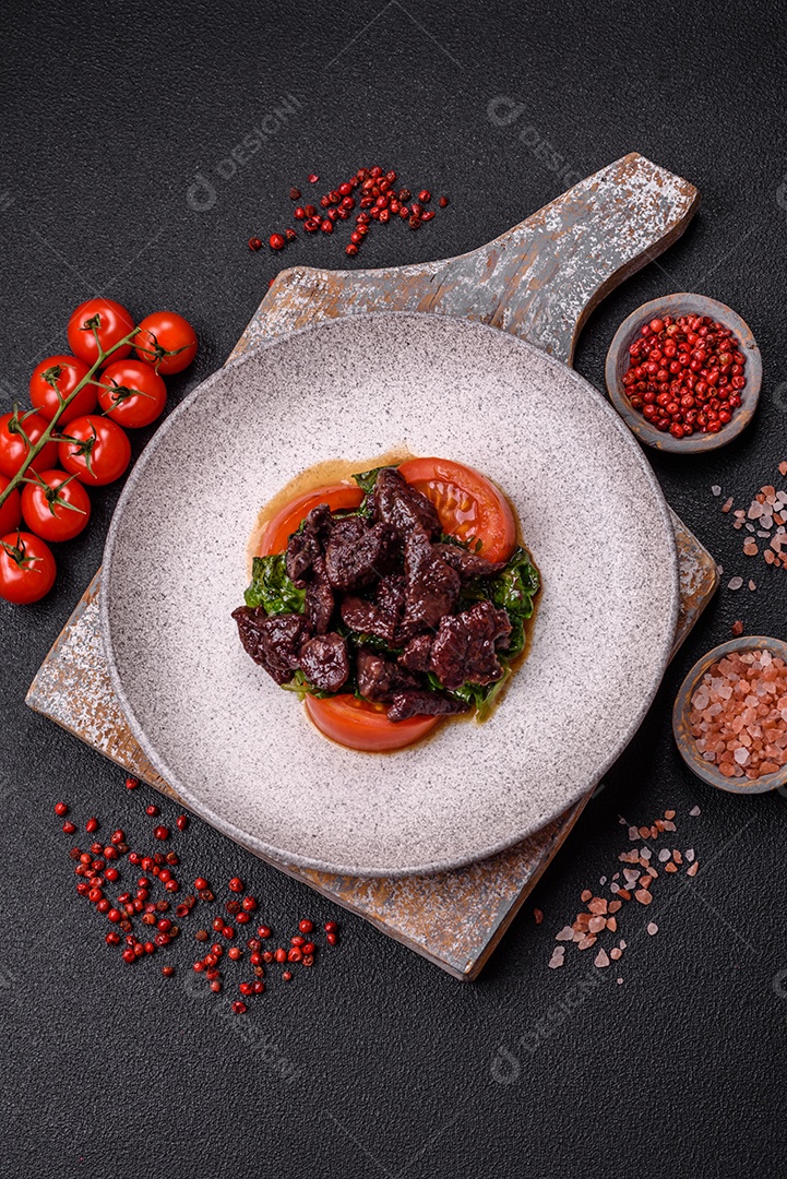 Deliciosa salada quente de fígado de galinha, espinafre, rúcula, tomate com sal, especiarias e ervas sobre um fundo escuro de concreto