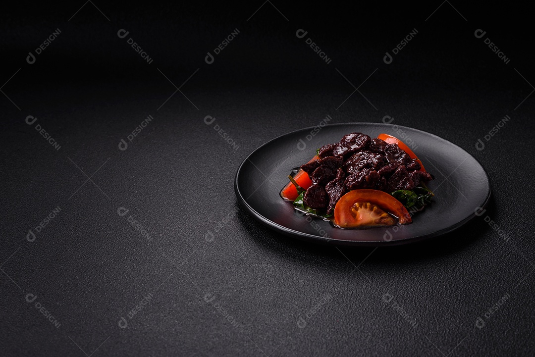 Deliciosa salada quente de fígado de galinha, espinafre, rúcula, tomate com sal, especiarias e ervas sobre um fundo escuro de concreto