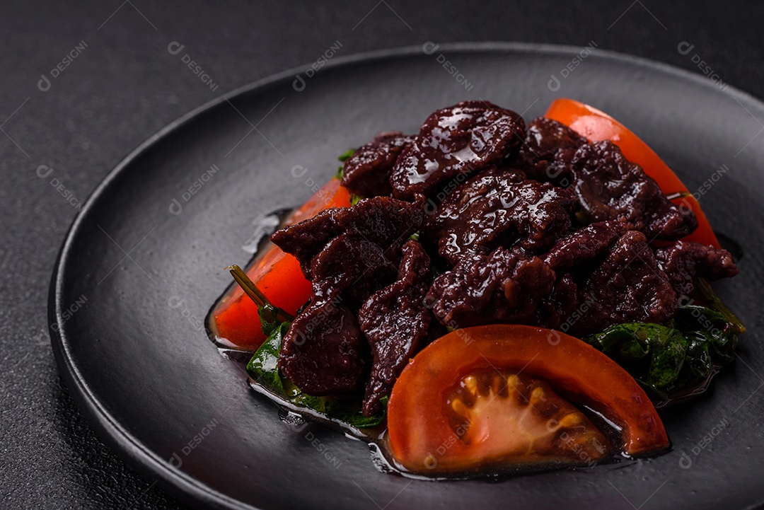 Deliciosa salada quente de fígado de galinha, espinafre, rúcula, tomate com sal, especiarias e ervas sobre um fundo escuro de concreto