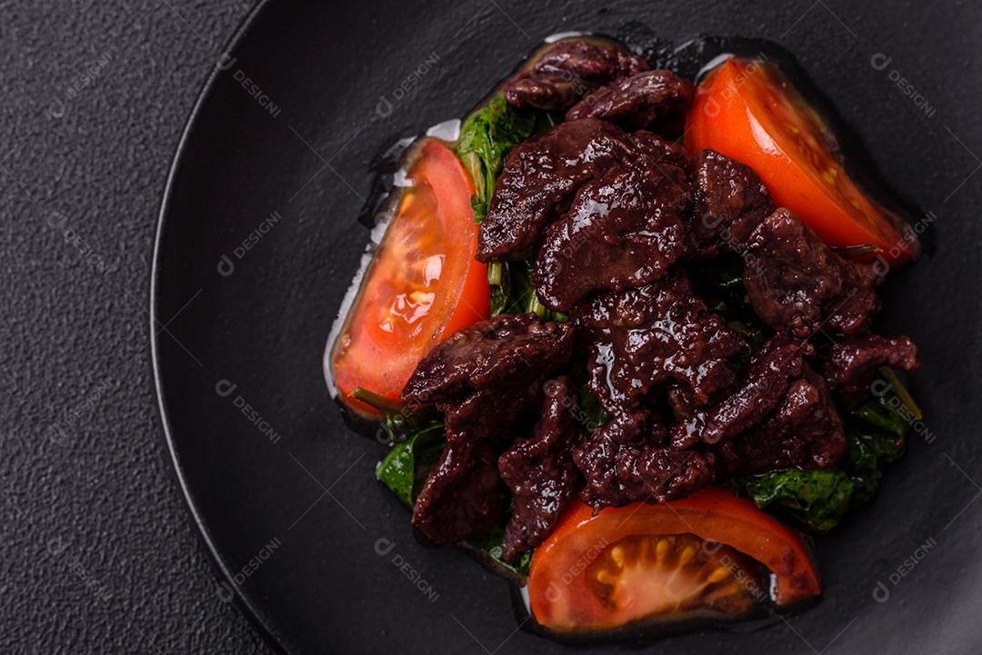 Deliciosa salada quente de fígado de galinha, espinafre, rúcula, tomate com sal, especiarias e ervas sobre um fundo escuro de concreto