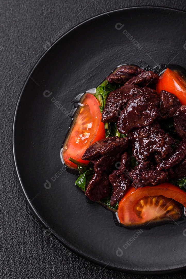 Deliciosa salada quente de fígado de galinha, espinafre, rúcula, tomate com sal, especiarias e ervas sobre um fundo escuro de concreto