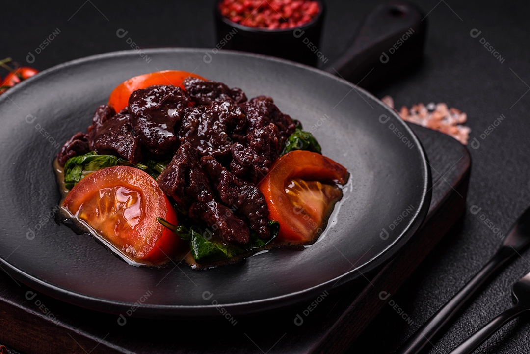 Deliciosa salada quente de fígado de galinha, espinafre, rúcula, tomate com sal, especiarias e ervas sobre um fundo escuro de concreto