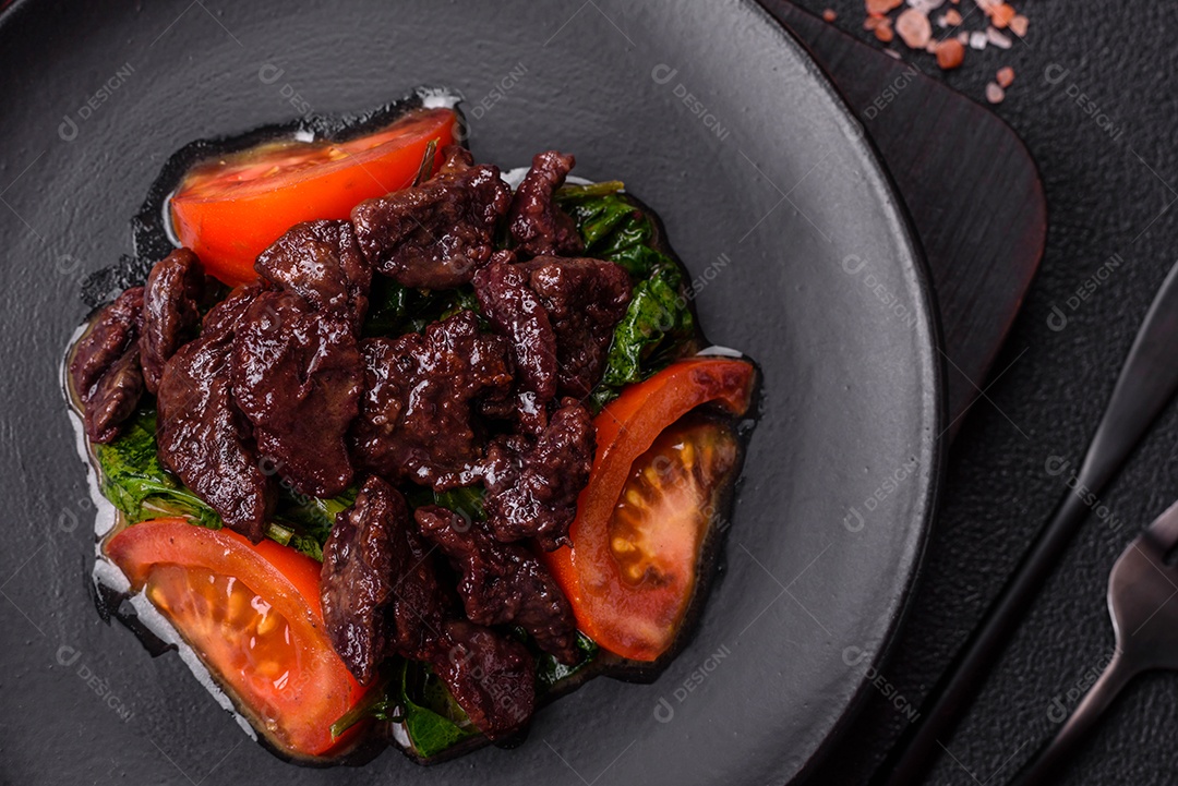 Deliciosa salada quente de fígado de galinha, espinafre, rúcula, tomate com sal, especiarias e ervas sobre um fundo escuro de concreto