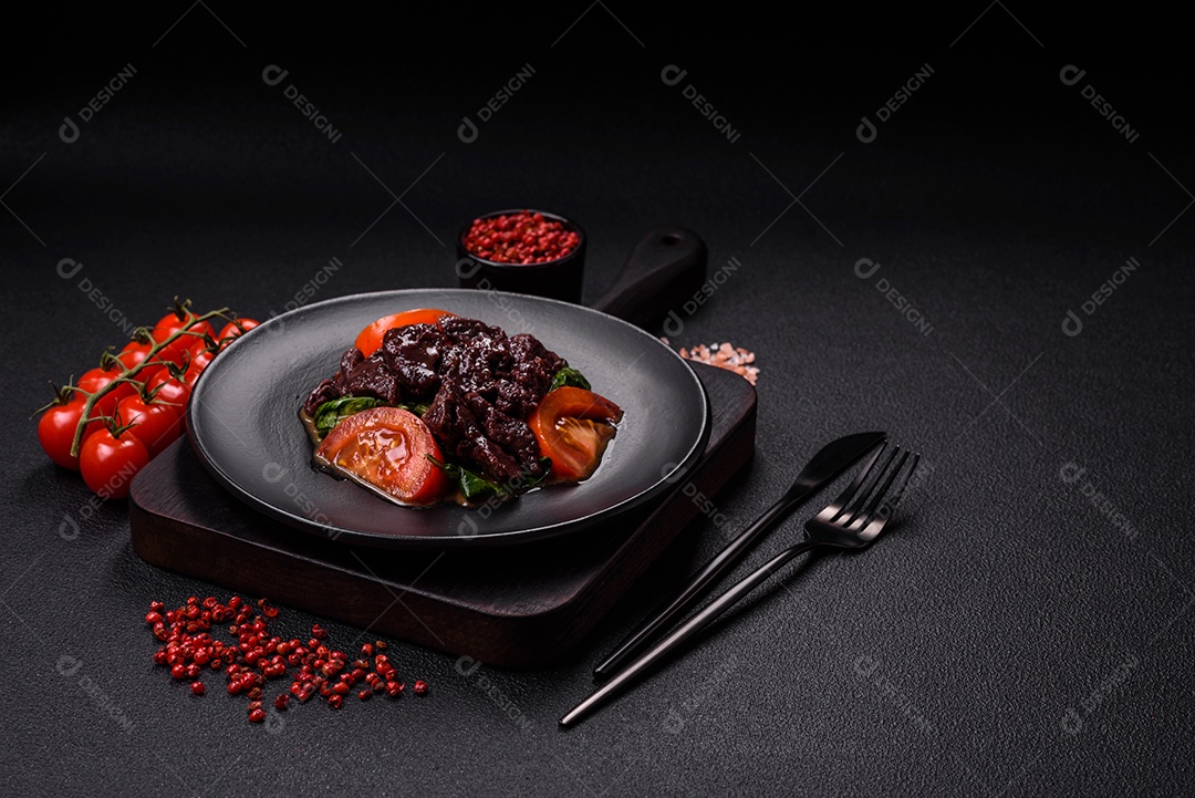 Deliciosa salada quente de fígado de galinha, espinafre, rúcula, tomate com sal, especiarias e ervas sobre um fundo escuro de concreto