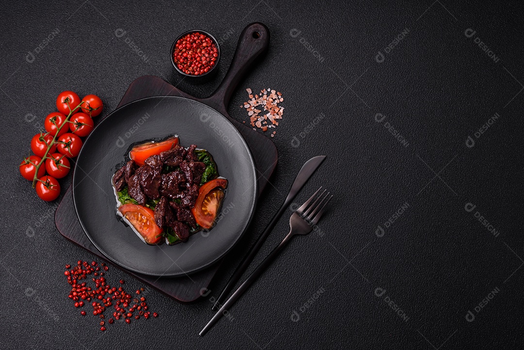 Deliciosa salada quente de fígado de galinha, espinafre, rúcula, tomate com sal, especiarias e ervas sobre um fundo escuro de concreto