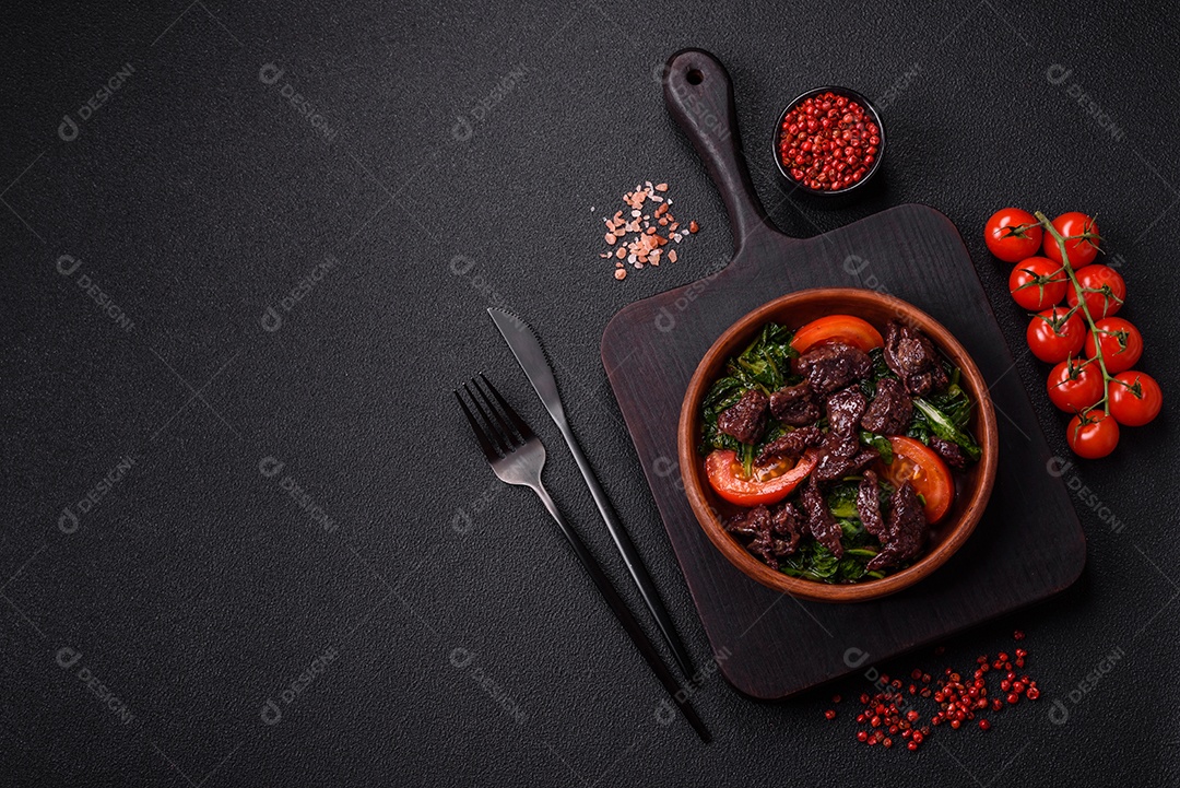 Deliciosa salada quente de fígado de galinha, espinafre, rúcula, tomate com sal, especiarias e ervas sobre um fundo escuro de concreto