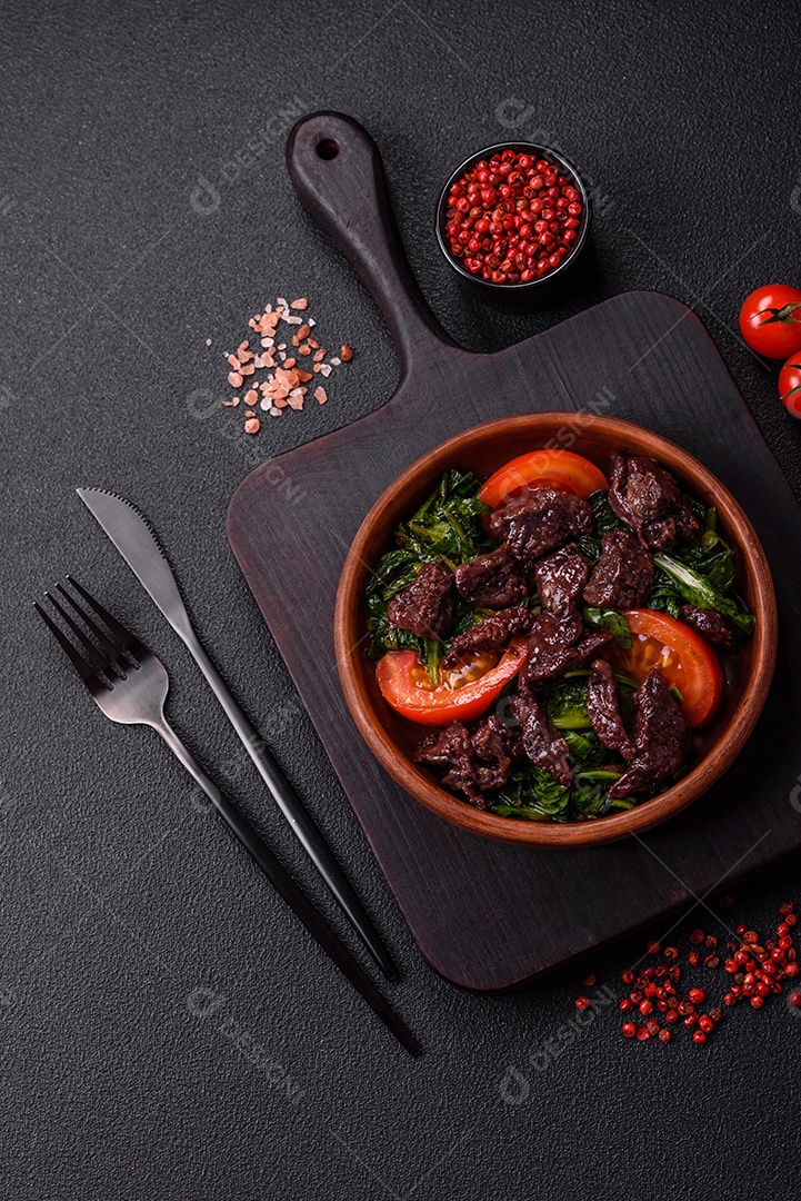 Deliciosa salada quente de fígado de galinha, espinafre, rúcula, tomate com sal, especiarias e ervas sobre um fundo escuro de concreto