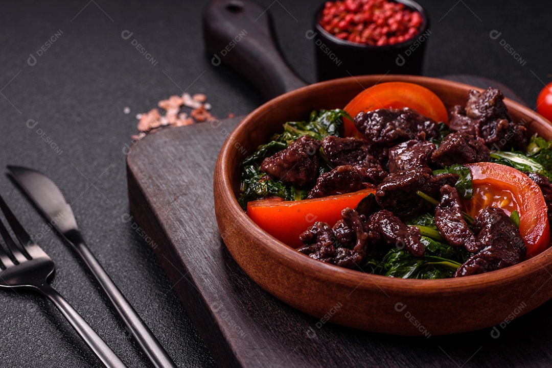 Deliciosa salada quente de fígado de galinha, espinafre, rúcula, tomate com sal, especiarias e ervas sobre um fundo escuro de concreto