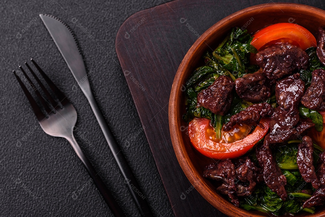 Deliciosa salada quente de fígado de galinha, espinafre, rúcula, tomate com sal, especiarias e ervas sobre um fundo escuro de concreto