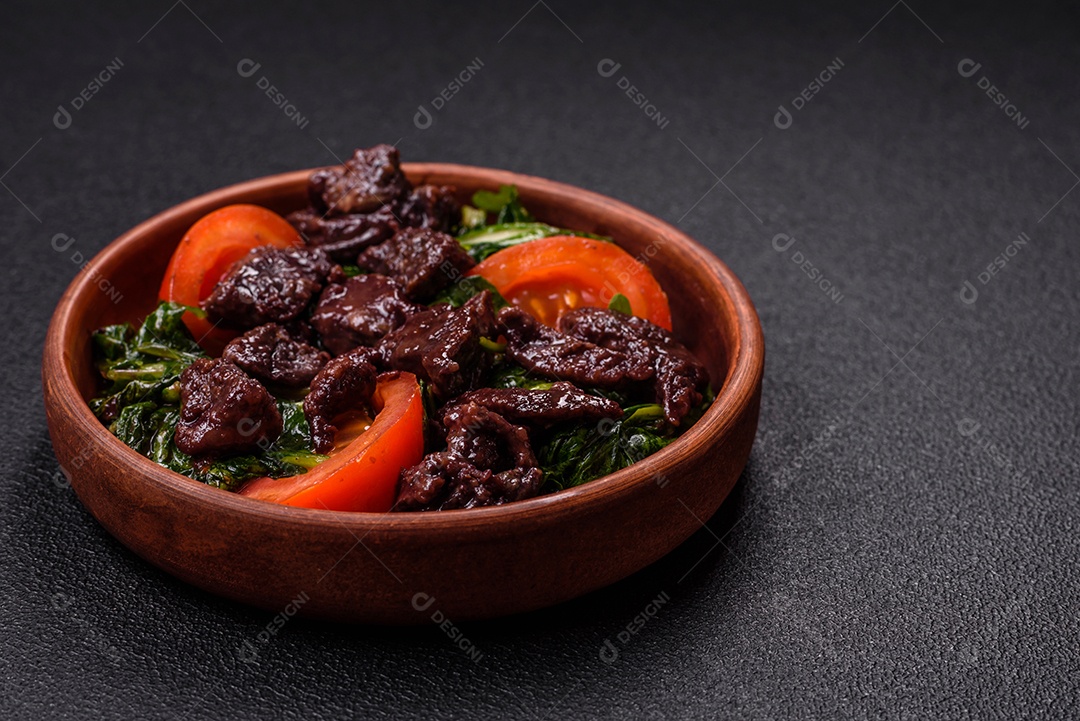 Deliciosa salada quente de fígado de galinha, espinafre, rúcula, tomate com sal, especiarias e ervas sobre um fundo escuro de concreto