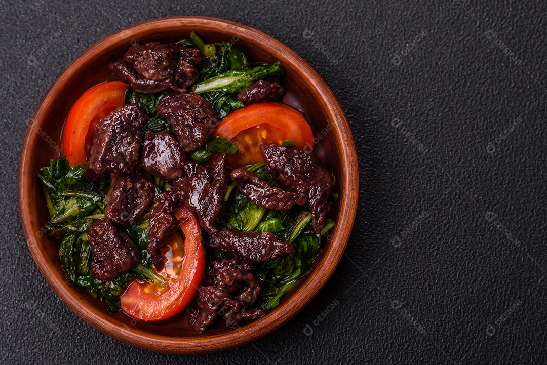 Deliciosa salada quente de fígado de galinha, espinafre, rúcula, tomate com sal, especiarias e ervas sobre um fundo escuro de concreto