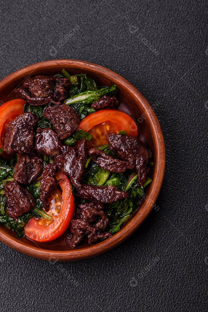 Deliciosa salada quente de fígado de galinha, espinafre, rúcula, tomate com sal, especiarias e ervas sobre um fundo escuro de concreto