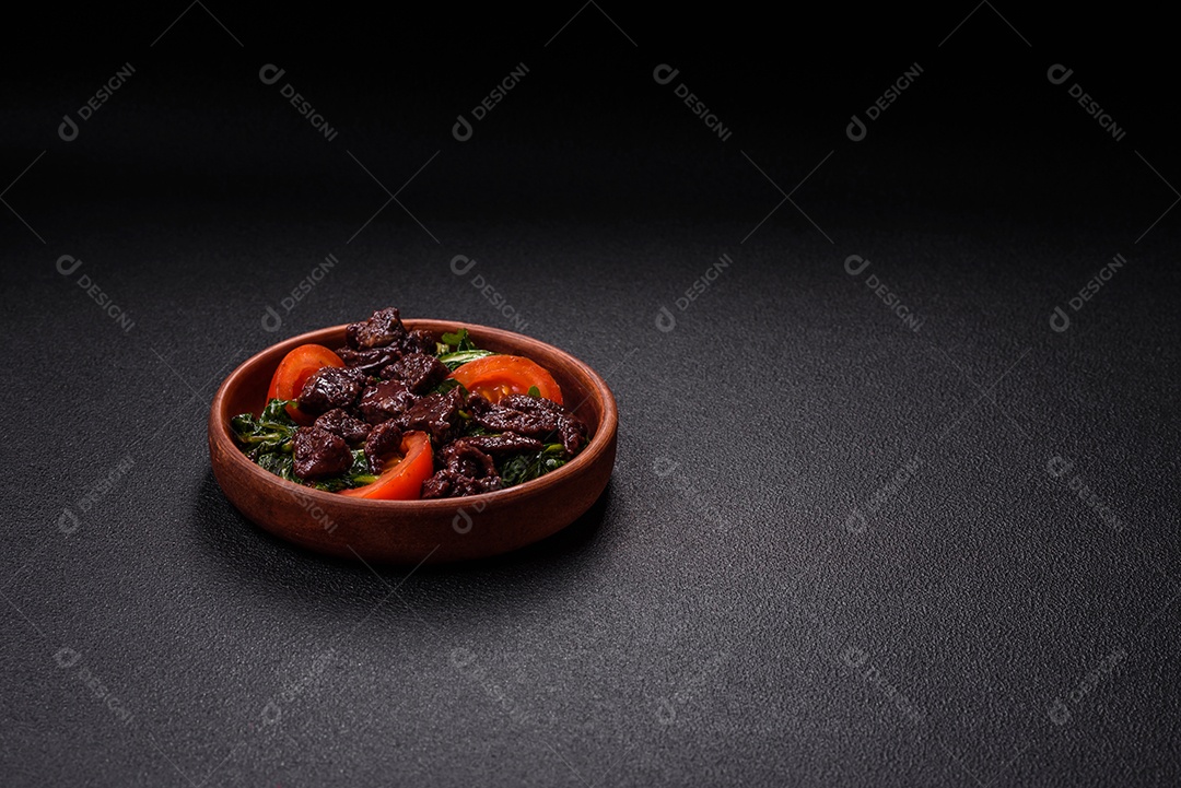 Deliciosa salada quente de fígado de galinha, espinafre, rúcula, tomate com sal, especiarias e ervas sobre um fundo escuro de concreto