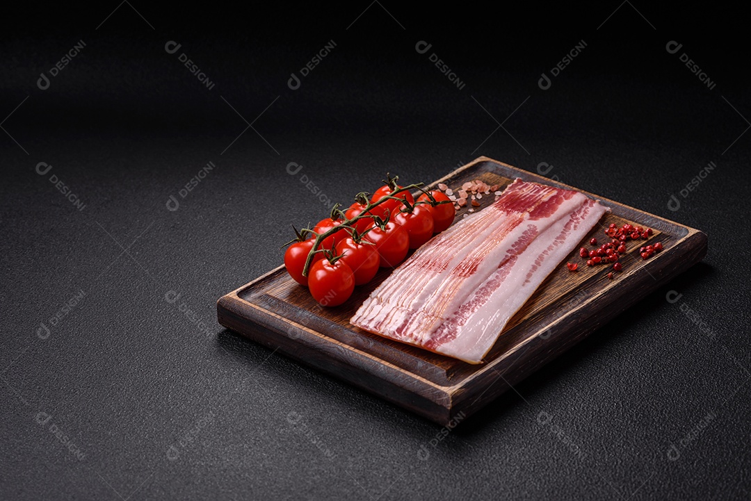 Delicioso bacon em forma de fatias com sal, especiarias e ervas sobre um fundo escuro de concreto