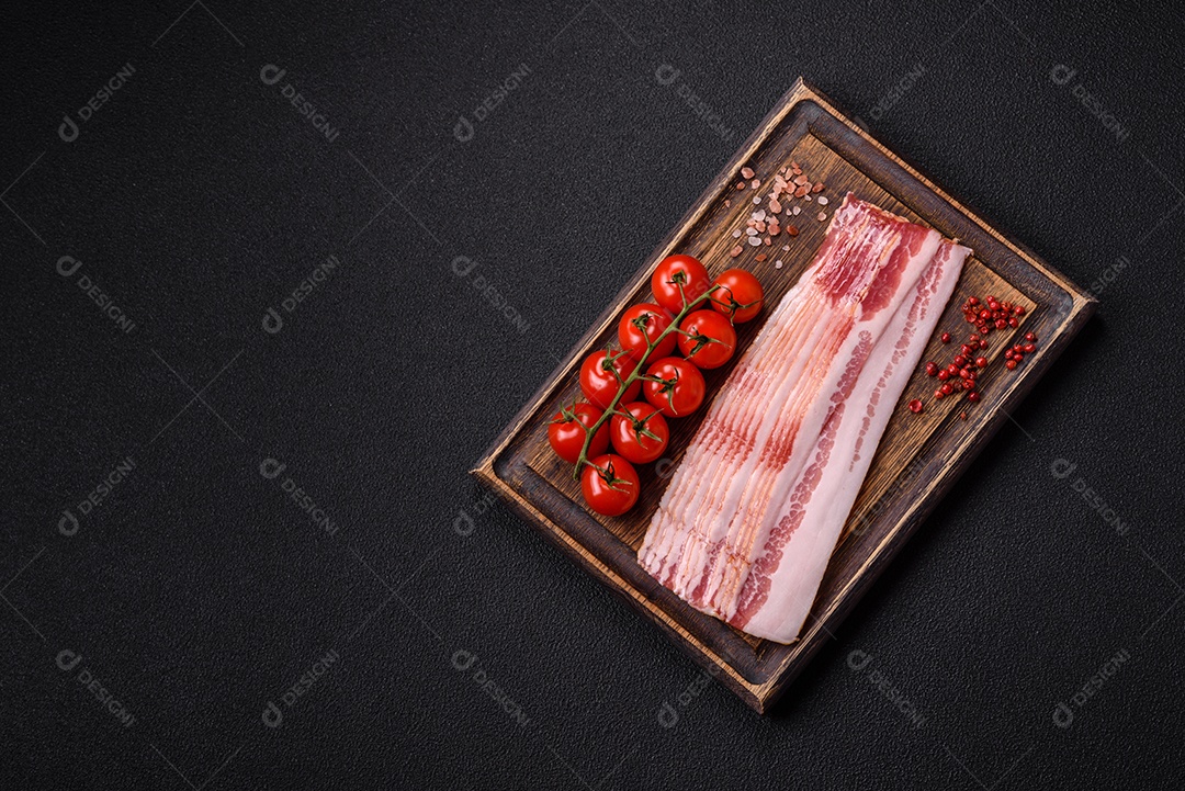 Delicioso bacon em forma de fatias com sal, especiarias e ervas sobre um fundo escuro de concreto