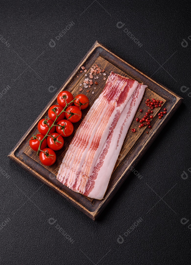 Delicioso bacon em forma de fatias com sal, especiarias e ervas sobre um fundo escuro de concreto