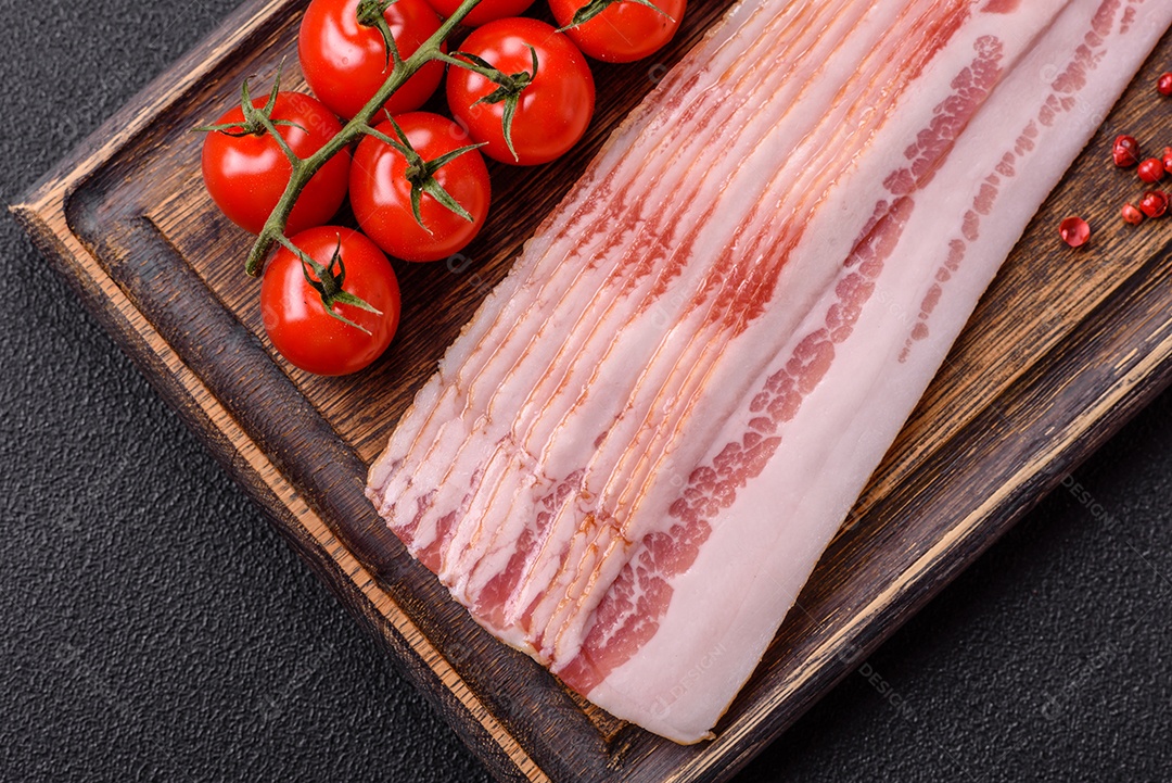 Delicioso bacon em forma de fatias com sal, especiarias e ervas sobre um fundo escuro de concreto