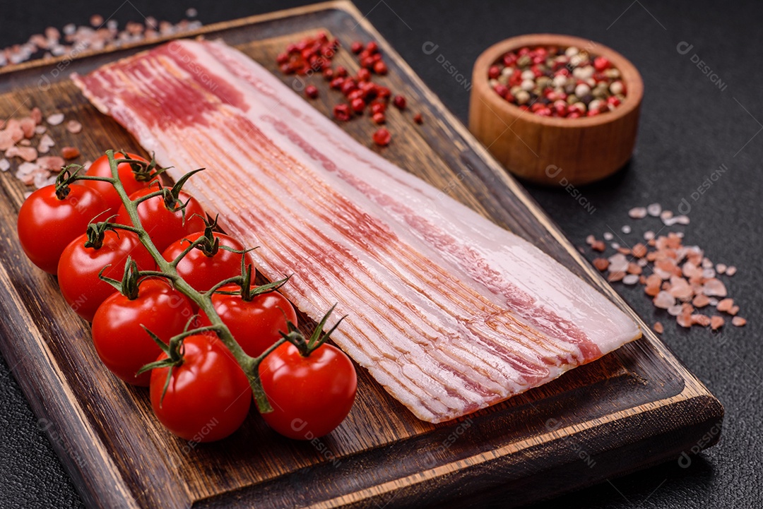Delicioso bacon em forma de fatias com sal, especiarias e ervas sobre um fundo escuro de concreto