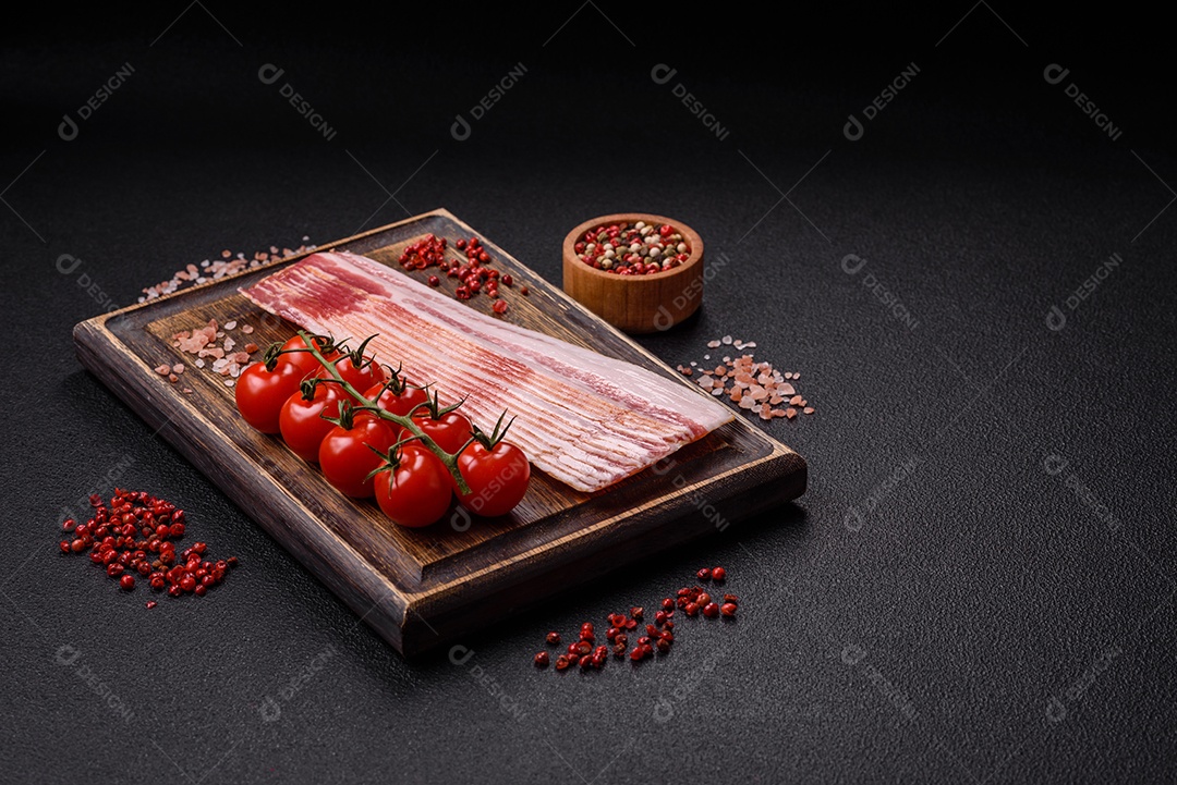 Delicioso bacon em forma de fatias com sal, especiarias e ervas sobre um fundo escuro de concreto