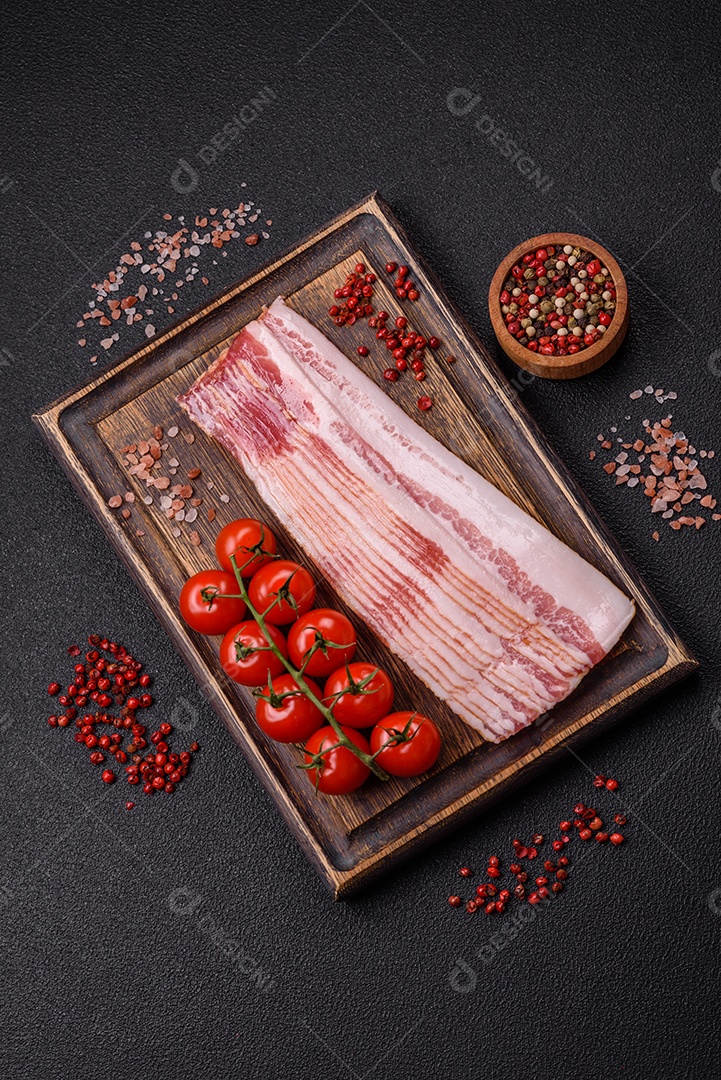 Delicioso bacon em forma de fatias com sal, especiarias e ervas sobre um fundo escuro de concreto