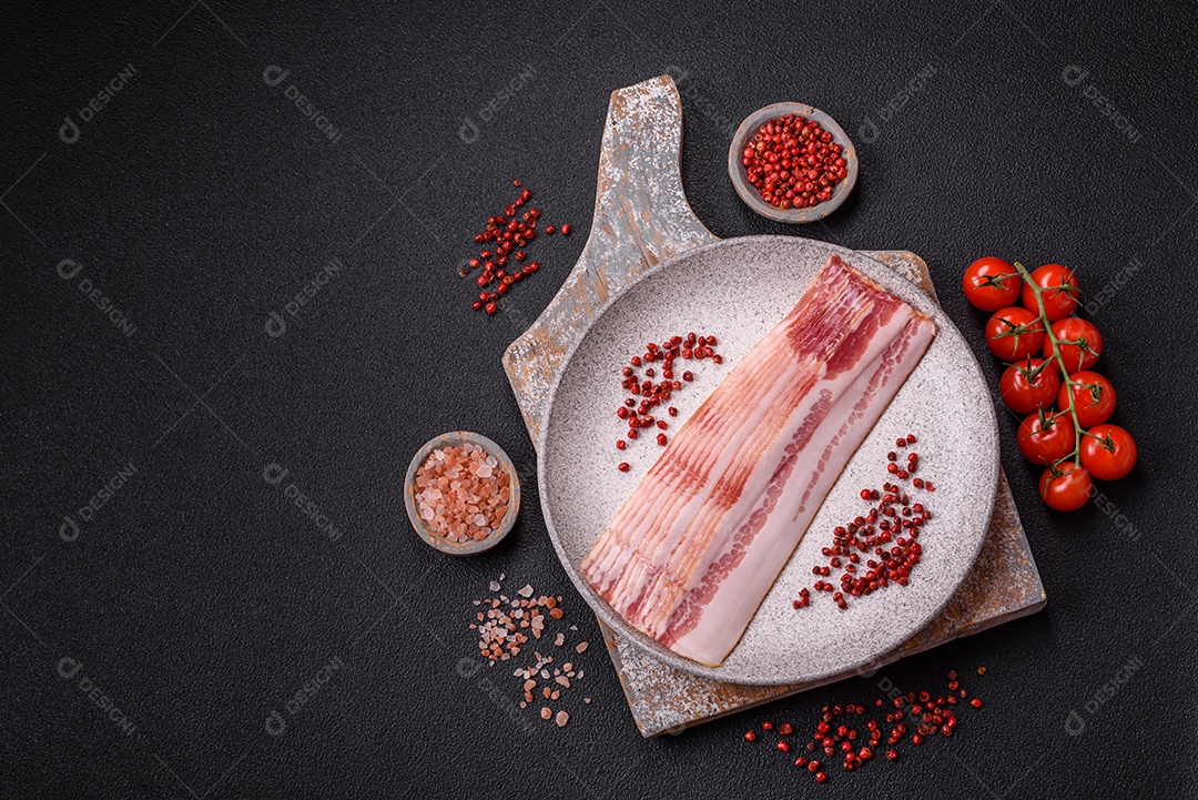 Delicioso bacon em forma de fatias com sal, especiarias e ervas sobre um fundo escuro de concreto
