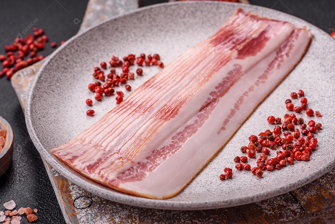 Delicioso bacon em forma de fatias com sal, especiarias e ervas sobre um fundo escuro de concreto