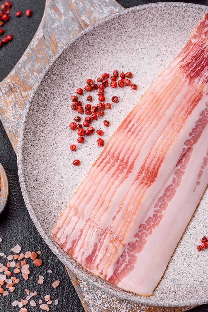 Delicioso bacon em forma de fatias com sal, especiarias e ervas sobre um fundo escuro de concreto