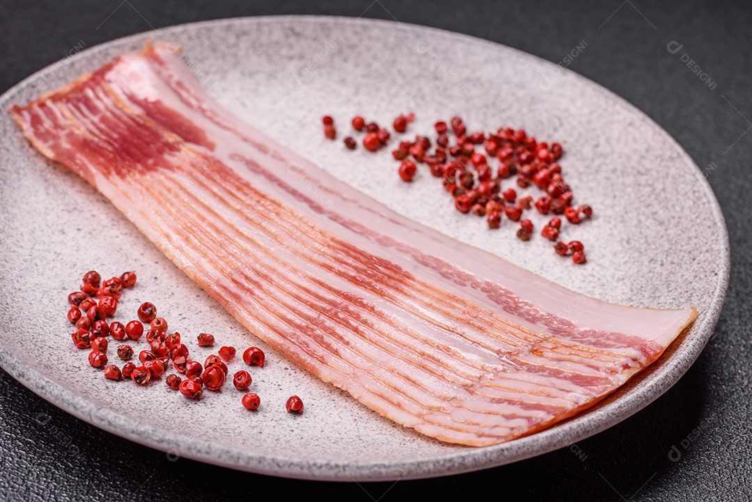 Delicioso bacon em forma de fatias com sal, especiarias e ervas sobre um fundo escuro de concreto