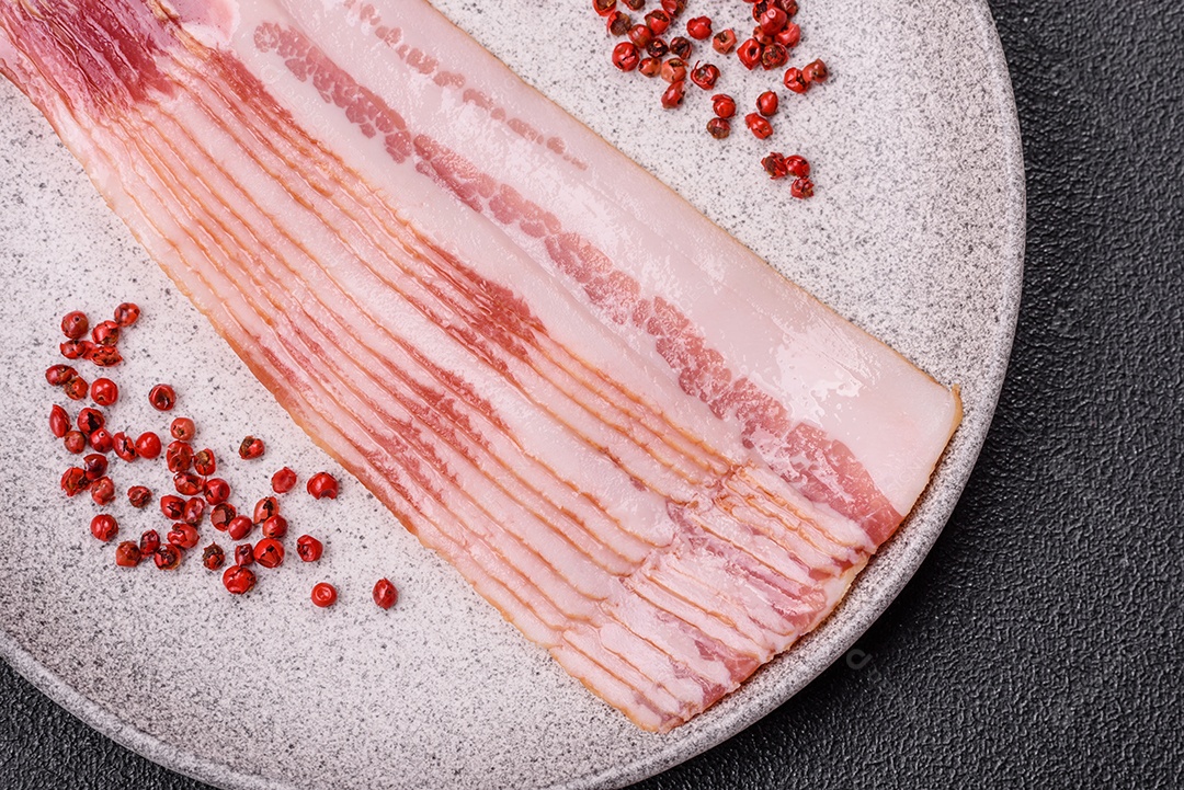 Delicioso bacon em forma de fatias com sal, especiarias e ervas sobre um fundo escuro de concreto