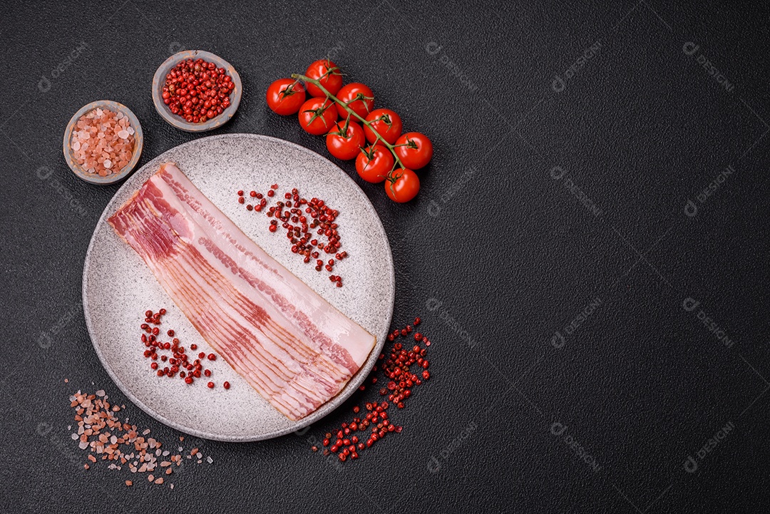 Delicioso bacon em forma de fatias com sal, especiarias e ervas sobre um fundo escuro de concreto
