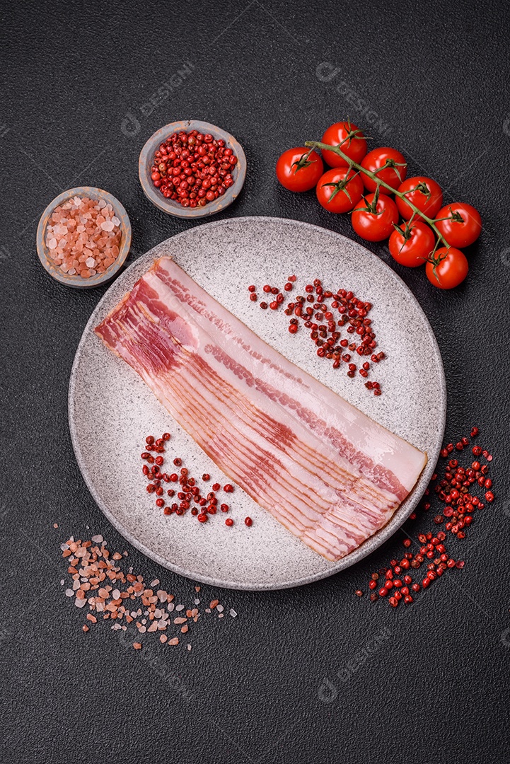 Delicioso bacon em forma de fatias com sal, especiarias e ervas sobre um fundo escuro de concreto