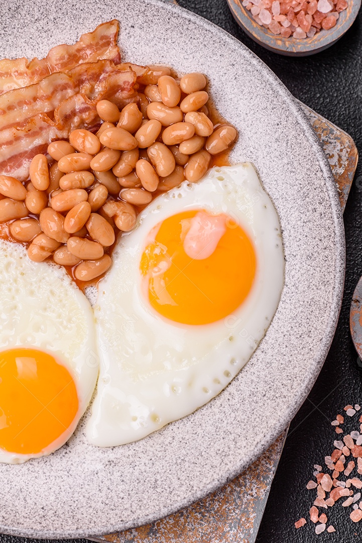 Café da manhã inglês com ovos fritos, bacon, feijão, tomate, especiarias e ervas. Um início de dia saudável e nutritivo