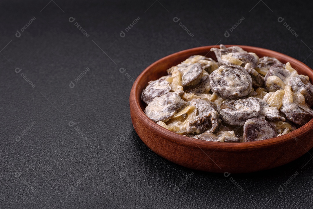 Corações de frango cozido cortados em fatias com cebola e molho cremoso com sal e especiarias sobre um fundo escuro de concreto