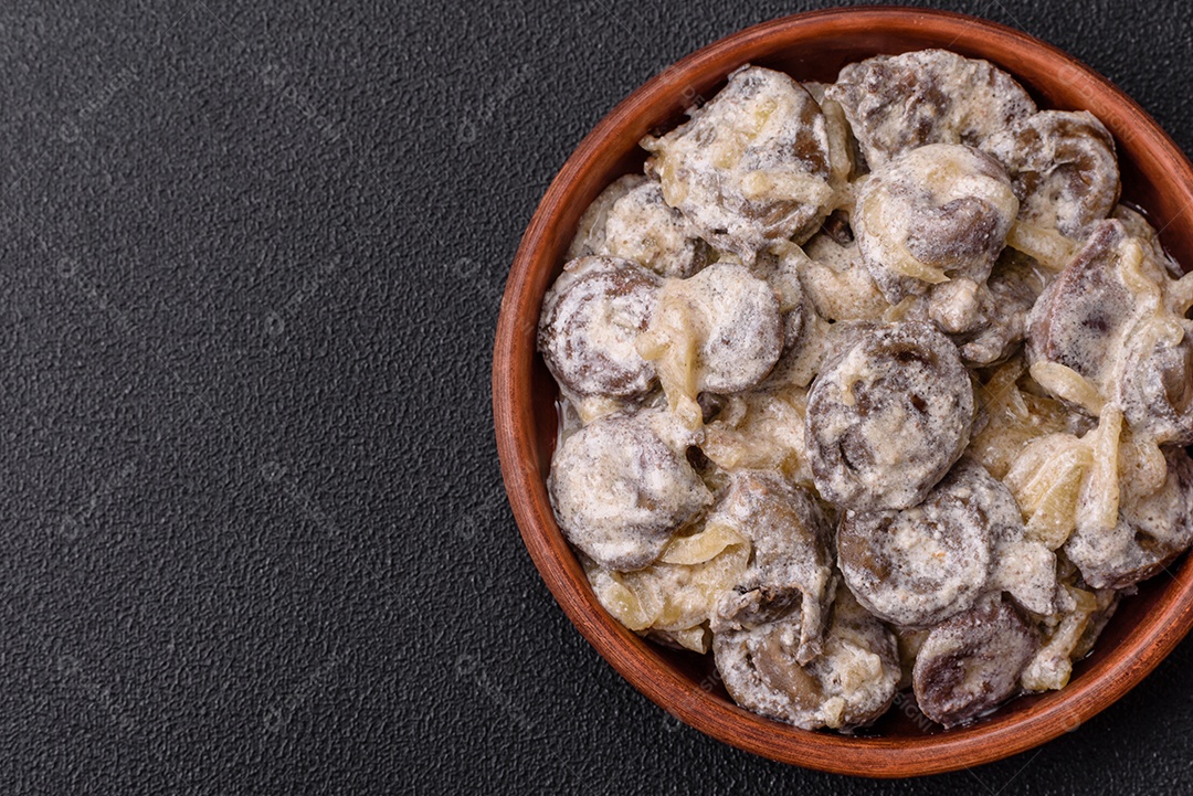 Corações de frango cozido cortados em fatias com cebola e molho cremoso com sal e especiarias sobre um fundo escuro de concreto