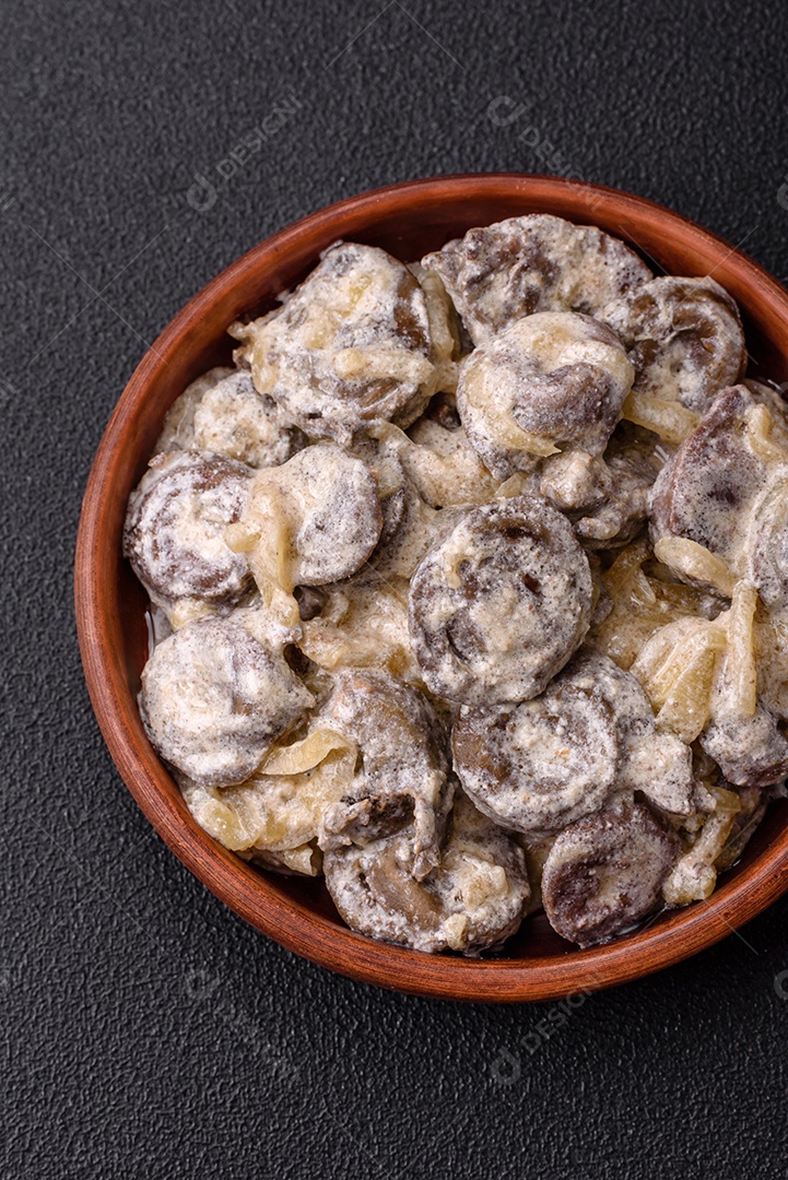 Corações de frango cozido cortados em fatias com cebola e molho cremoso com sal e especiarias sobre um fundo escuro de concreto