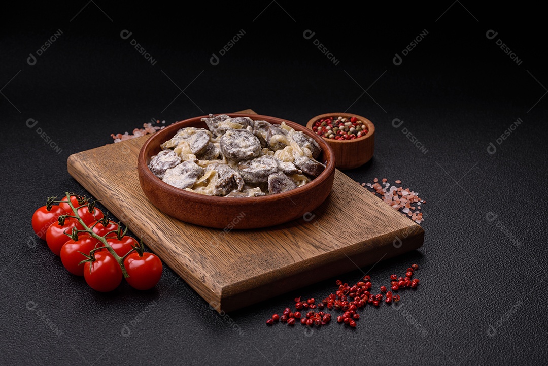Corações de frango cozido cortados em fatias com cebola e molho cremoso com sal e especiarias sobre um fundo escuro de concreto