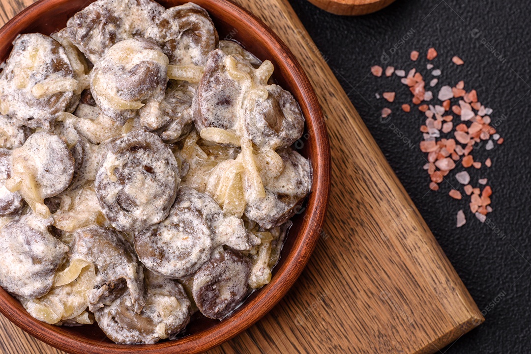 Corações de frango cozido cortados em fatias com cebola e molho cremoso com sal e especiarias sobre um fundo escuro de concreto