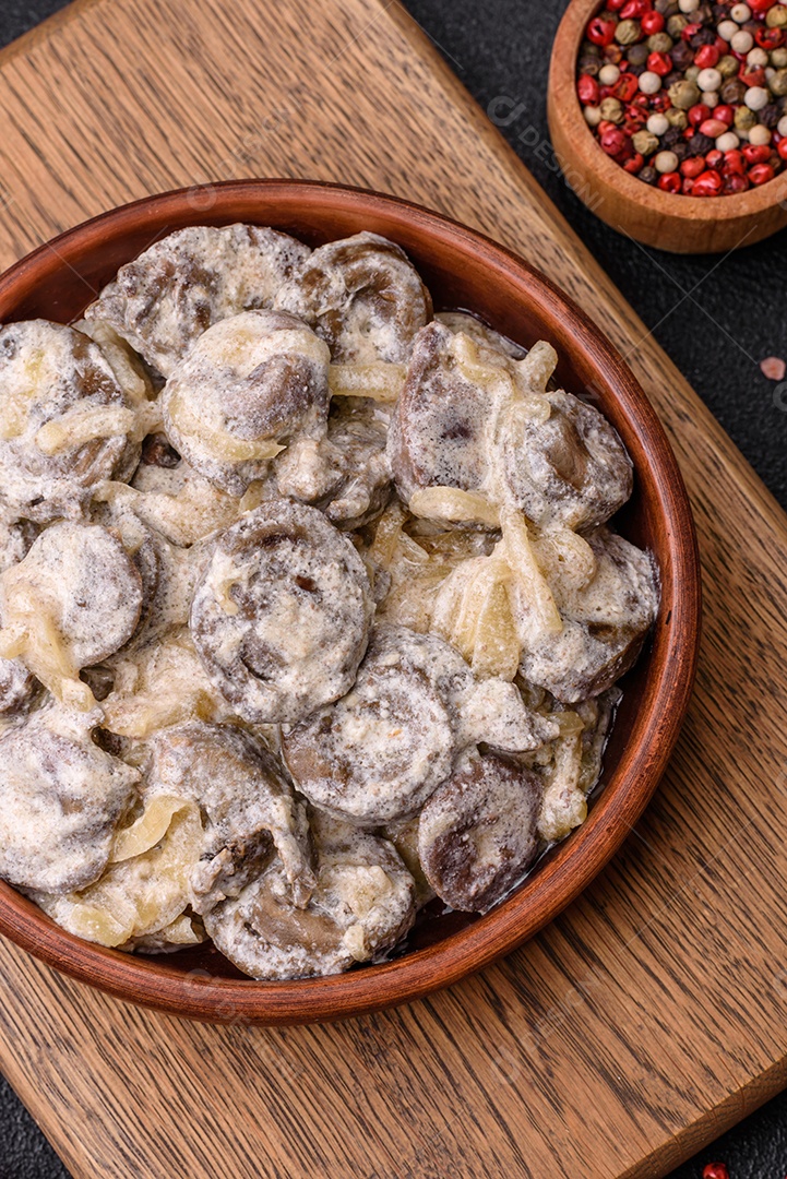 Corações de frango cozido cortados em fatias com cebola e molho cremoso com sal e especiarias sobre um fundo escuro de concreto